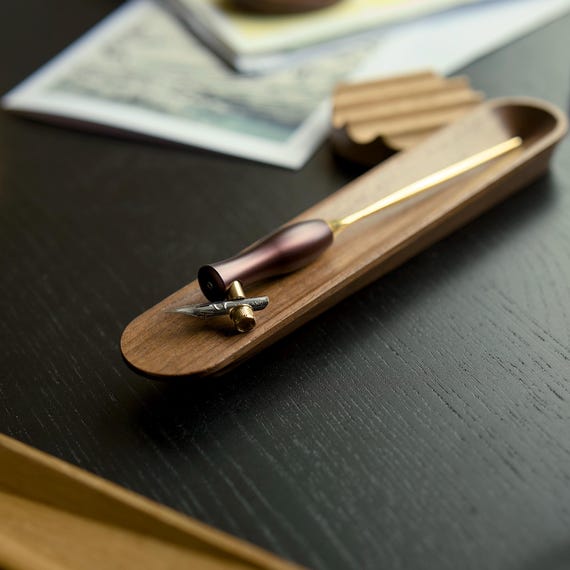 A beautifully minimal walnut pen rest that turns a humble writing tool into a displayed object — the kind of quiet craft upgrade a serious desk person actually notices.