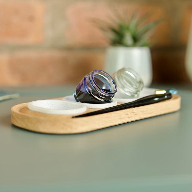 May include: A wooden tray with three small glass jars, two with clear liquid and one with blue ink. A black calligraphy pen is on the tray.
