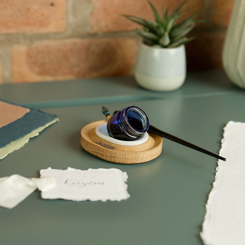May include: A wooden inkwell with a blue glass ink bottle and a black calligraphy pen. The inkwell is on a green surface with a piece of white paper and a handwritten note that says "Love you".