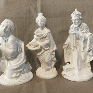 Può includere: Tre statuette in ceramica bianca raffiguranti i Re Magi biblici. Uno è in ginocchio con un vaso, un altro porta un piatto e il terzo è in piedi con una lanterna. Le figure sono dettagliate con vesti e barbe, per un presepe.