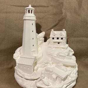 May include: A white ceramic lighthouse sculpture. It features a tall tower, a small house, and a boat. The lighthouse has a detailed design with windows and a light at the top. The sculpture sits on a rocky base.