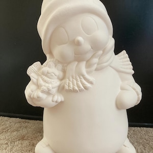 Può includere: Figurina di pupazzo di neve in ceramica bianca con cappello e sciarpa, che tiene un piccolo uccello nella mano sinistra. Il pupazzo di neve ha un sorriso e occhi dipinti.