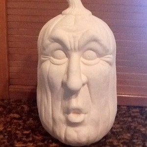May include: White ceramic pumpkin with a carved face, featuring a wide mouth, large eyes, and a furrowed brow. The pumpkin is unpainted and ready for decorating.