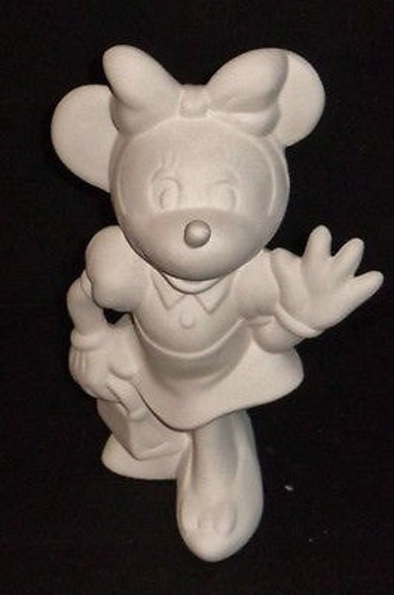 Puede incluir: Figura de cer&aacute;mica blanca de un rat&oacute;n de dibujos animados con un vestido y un lazo. El rat&oacute;n sostiene un libro y saluda con una mano.