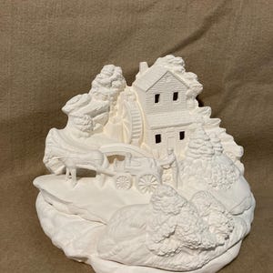 May include: A white ceramic ornament showing a rural scene. It features a two-storey house with a water wheel, a horse-drawn carriage, and sculpted trees. The ornament is unpainted and ready for customisation.