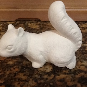 May include: A white ceramic squirrel figurine with a large, curved tail. The squirrel is in a sitting position, with its front paws close to its body. The figurine is unpainted and ready for customization.