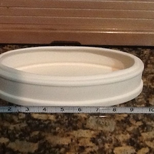 Peut inclure: Plat en céramique de forme ovale blanche avec un bord surélevé. Le plat mesure environ 23 cm de long.