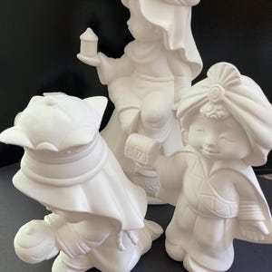 Op de afbeelding: Drie witte keramische beeldjes van de drie wijzen uit het oosten, elk met een unieke hoofdbedekking en een geschenk. De beeldjes zijn klaar om te worden beschilderd.