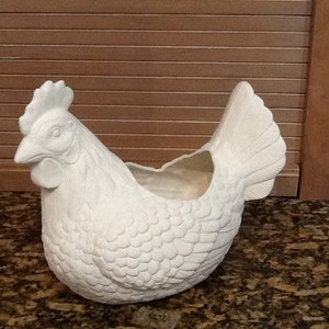 May include: White ceramic chicken planter with a detailed feathered design. The planter has a hollowed-out space in the back for planting.