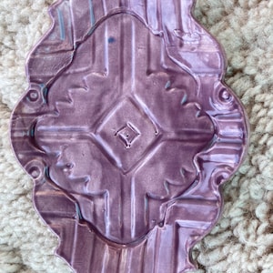 Puede incluir: Un plato de cerámica morado con un diseño decorativo. El plato tiene un borde festoneado y un centro elevado.