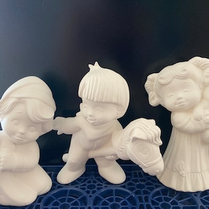 Könnte beinhalten: Drei weiße Keramikfiguren von Kindern. Ein Kind hält ein Spielzeugpferd, ein anderes ein kleines Tier und das dritte ein kleines Objekt.