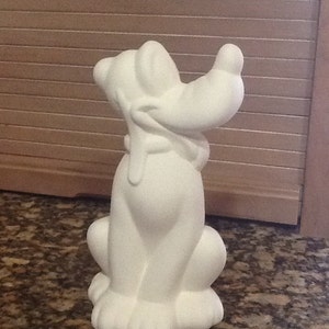 May include: White ceramic figurine of a dog sitting with its head tilted back. The dog has large ears and a long snout.