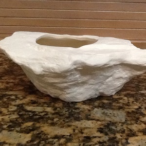 Puede incluir: Maceta de cerámica blanca con forma de roca con un interior liso y redondeado.