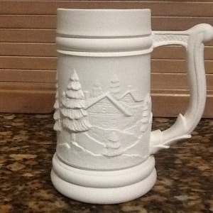 May include: White ceramic beer stein featuring a raised design of a cabin and trees. The stein has a handle and a wide base.