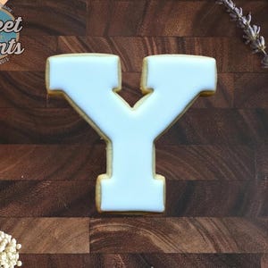 May include: A letter Y shaped sugar cookie with smooth white icing. The cookie features the Sweet Prints logo in the top left corner, which includes the text Sweet Prints Established 2015 and Elevate your baking.