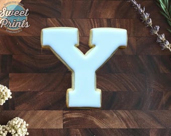 May include: A letter Y shaped sugar cookie with smooth white icing. The cookie features the Sweet Prints logo in the top left corner, which includes the text Sweet Prints Established 2015 and Elevate your baking.