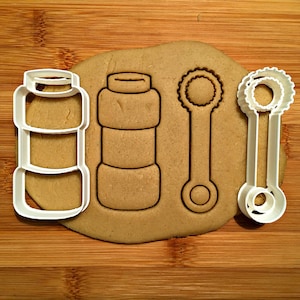 May include: Cookie cutters in the shape of a bubble bottle and wands. The white plastic cutters are on a piece of dough, with the impressions of the shapes visible. The dough is on a wooden surface.