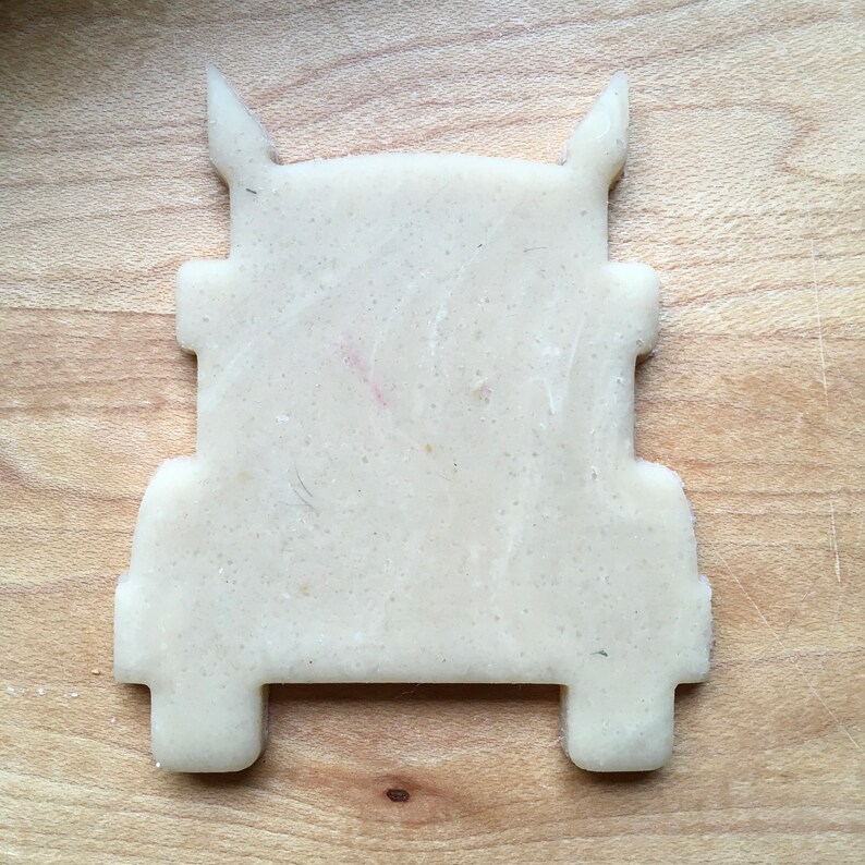 May include: A white cookie cutter in the shape of a semi-truck. The cutter is made of plastic and has a smooth surface.