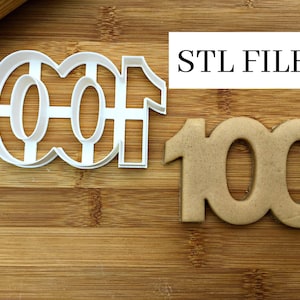 Puede incluir: Un cortador de galletas de plástico blanco con la forma del número 100 junto a una galleta horneada con la misma forma. El texto "STL FILE" está en un rectángulo blanco. Los artículos están sobre una superficie de madera.