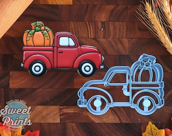 May include: A red truck cookie with an orange pumpkin in the bed, featuring white windows and black wheels, alongside a light blue plastic cookie cutter shaped like a truck carrying a pumpkin, with the Sweet Prints logo visible in the corner.