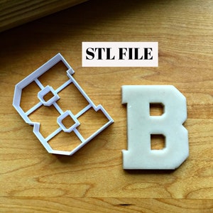 May include: A white plastic cookie cutter in the shape of the letter B. The cutter is on a wooden surface next to a white fondant cookie in the shape of the letter B. The text "STL FILE" is printed on a white rectangle.