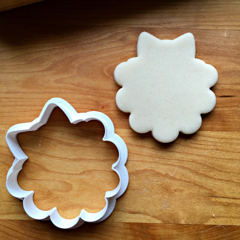 May include: A white plastic cookie cutter shaped like a flower with a white unbaked cookie in the background.