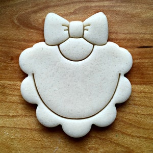 May include: White cookie cutter shaped like a baby bib with a bow on top.