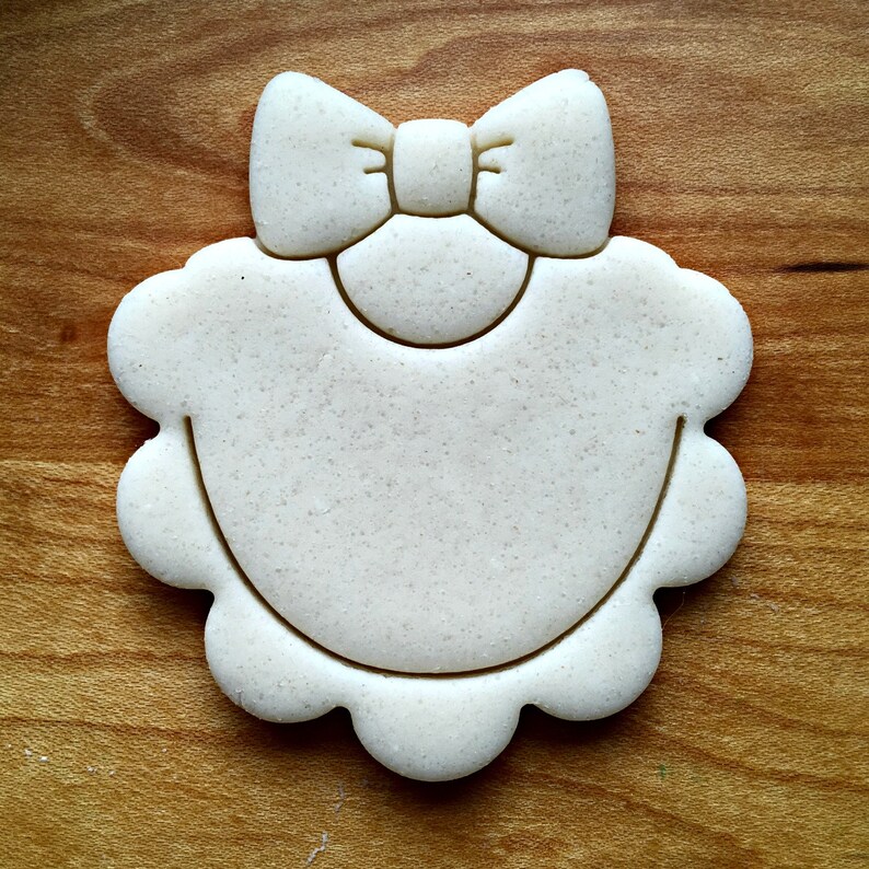 May include: White cookie cutter shaped like a baby bib with a bow on top.