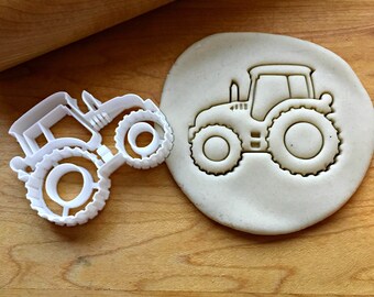 May include: White plastic tractor cookie cutter with a rolled out piece of dough showing the impression of the cutter.