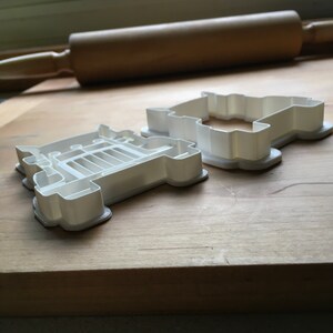 May include: Two white plastic cookie cutters shaped like a truck. The cutters are on a wooden surface.