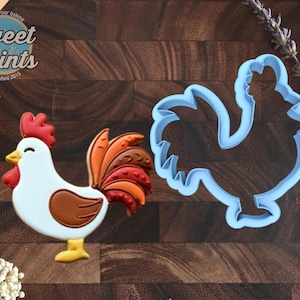 May include: A rooster-shaped cookie decorated with white icing, a red comb and wattle, a yellow beak, and a brown wing with a multi-colored tail in shades of orange, red, and brown, alongside a light blue plastic rooster-shaped cookie cutter.