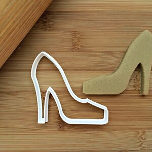 May include: White plastic high heel shoe cookie cutter on a wooden surface.