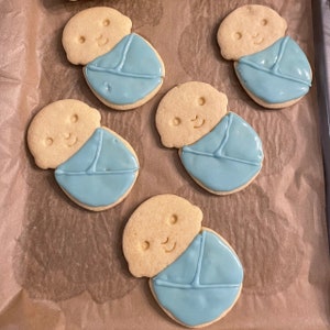 May include: Five sugar cookies decorated with blue icing to look like babies swaddled in blankets.