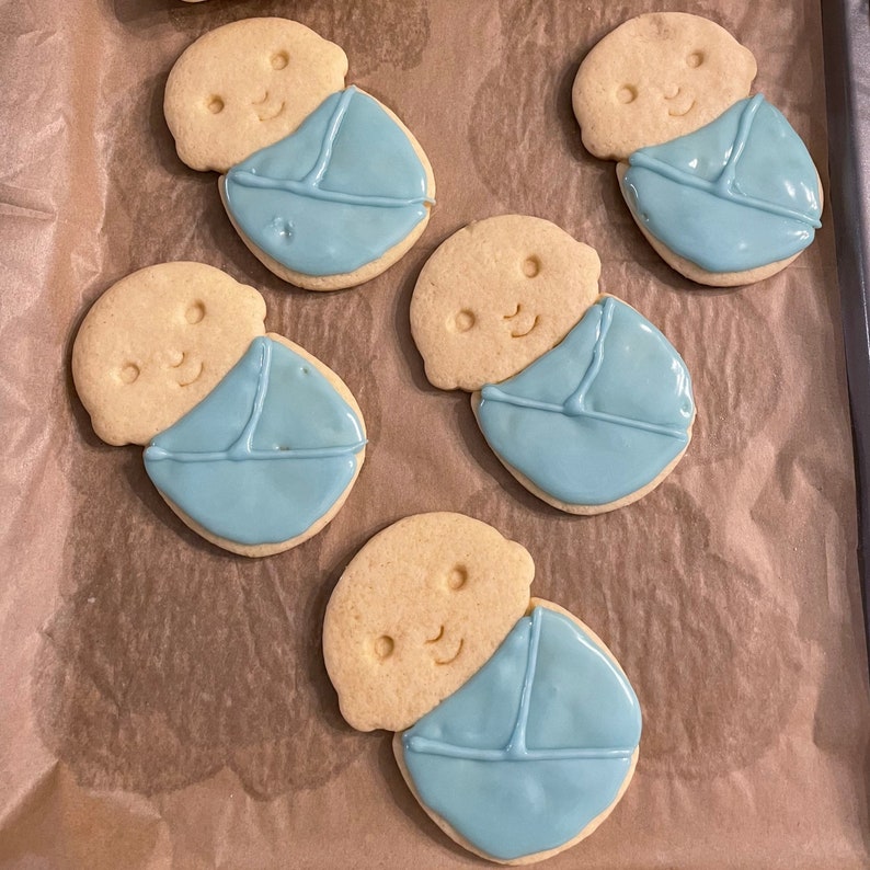 May include: Five sugar cookies decorated with blue icing to look like babies swaddled in blankets.