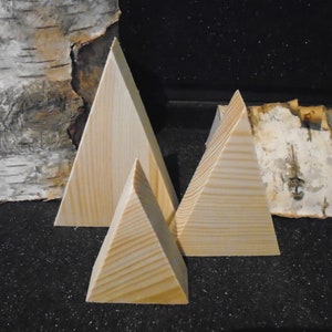 May include: Three wooden triangular shapes, made of light wood, arranged in a pyramid shape on a black surface. The largest triangle is at the back, with a smaller triangle in front of it, and the smallest triangle in front of that.
