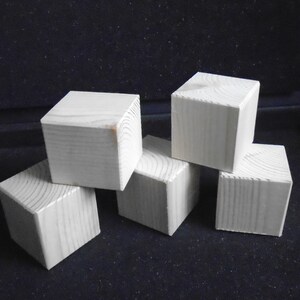 May include: Five white wooden blocks stacked on top of each other. The blocks are all the same size and shape, and they are made of a light-coloured wood.