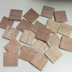 May include: A collection of small, square wooden tiles in varying shades of brown and tan. The tiles have visible wood grain patterns, with some appearing lighter and others darker. The tiles are scattered on a light-coloured surface.