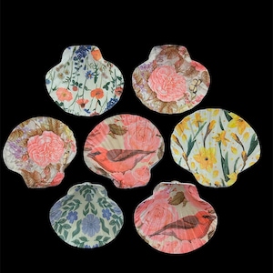 May include: A collection of seven decorative scallop shells featuring various decoupage designs. The patterns include vibrant floral arrangements with poppies, pink roses, and yellow daffodils, alongside illustrations of red birds on a light background.