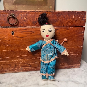 Puede incluir: Una muñeca de tela hecha a mano vestida con un atuendo estampado en azul y dorado. La muñeca tiene una pieza de pelo negro y una cara pintada.