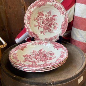 Puede incluir: Un conjunto de cuencos de cerámica blanca con un estampado floral rojo y bordes festoneados. Los cuencos presentan un diseño de flores y pájaros. Los cuencos se exhiben sobre un barril de madera.