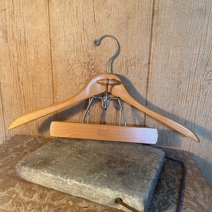 May include: A wooden hanger with a metal hook and a wooden bar. The hanger is resting on a gray stone surface.