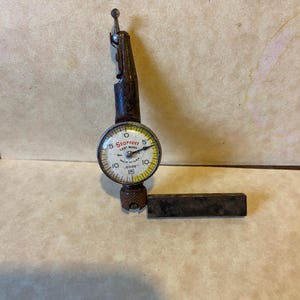 May include: A vintage Starrett dial indicator with a black and silver finish. The dial is yellow with black markings and reads 0 to 15 in increments of 0.0005. The indicator is made in the USA.
