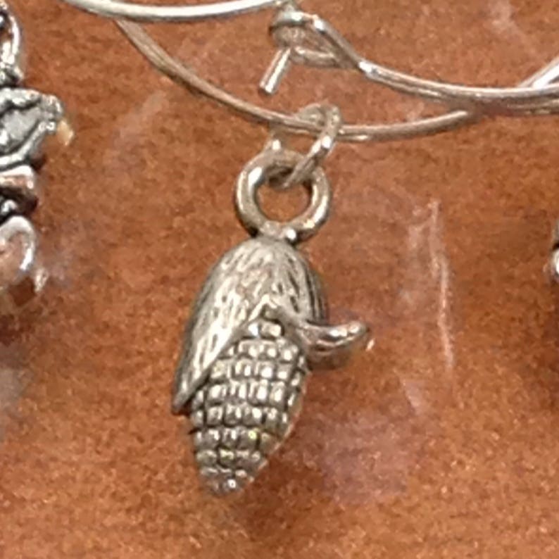 May include: Silver charm in the shape of an ear of corn. The charm is detailed with a husk and kernels.