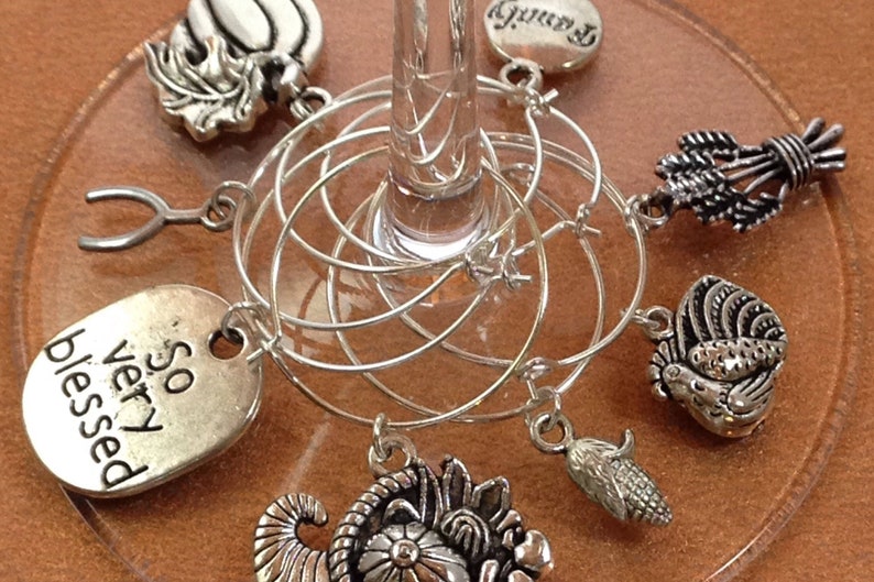 May include: Set of six silver wine glass charms with various Thanksgiving-themed designs, including a turkey, cornucopia, and a sign that reads "So very blessed".