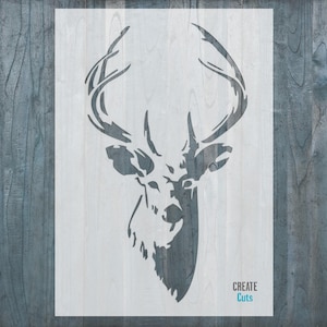 May include: A white stencil of a deer head with large antlers. The stencil is on a blue wood background. The text "CREATE Cuts" is in the bottom right corner.