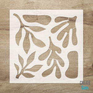 May include: White stencil featuring an abstract design of leaves and branches. The stencil is displayed against a wooden background. The text "CREATE Cuts" appears in the bottom right corner.