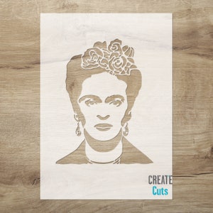 May include: White stencil of Frida Kahlo's face with a flower crown. The stencil is on a wood background. The text "CREATE Cuts" is at the bottom of the stencil.