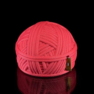 Pu&ograve; includere: Un contenitore rosso, sferico, simile a un gomitolo di lana. Il contenitore &egrave; realizzato in un materiale strutturato e ha un coperchio incernierato. Un piccolo fermaglio color oro chiude il coperchio. Lo sfondo &egrave; nero.