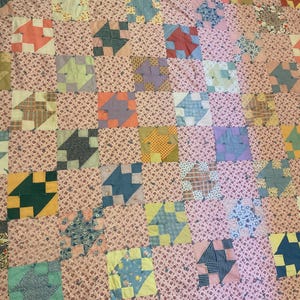 May include: A patchwork quilt featuring a repeating grid of alternating squares. One set of squares consists of a light pink fabric with a small floral pattern, while the other set contains various geometric blocks in blue, green, yellow, and orange.