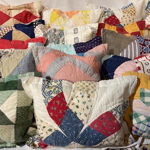 May include: A collection of rectangular throw pillows featuring various patchwork quilt designs. The pillows display a wide array of colors, including red, green, yellow, blue, and white, with diverse patterns such as floral, plaid, and geometric shapes.